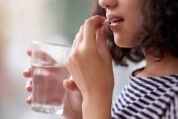 Frau in quergestreiften T-Shirt führt sich Tablette zum Mund, Glas Wasser in der anderen Hand Frau in quergestreiften T-Shirt führt sich Tablette zum Mund, Glas Wasser in der anderen Hand